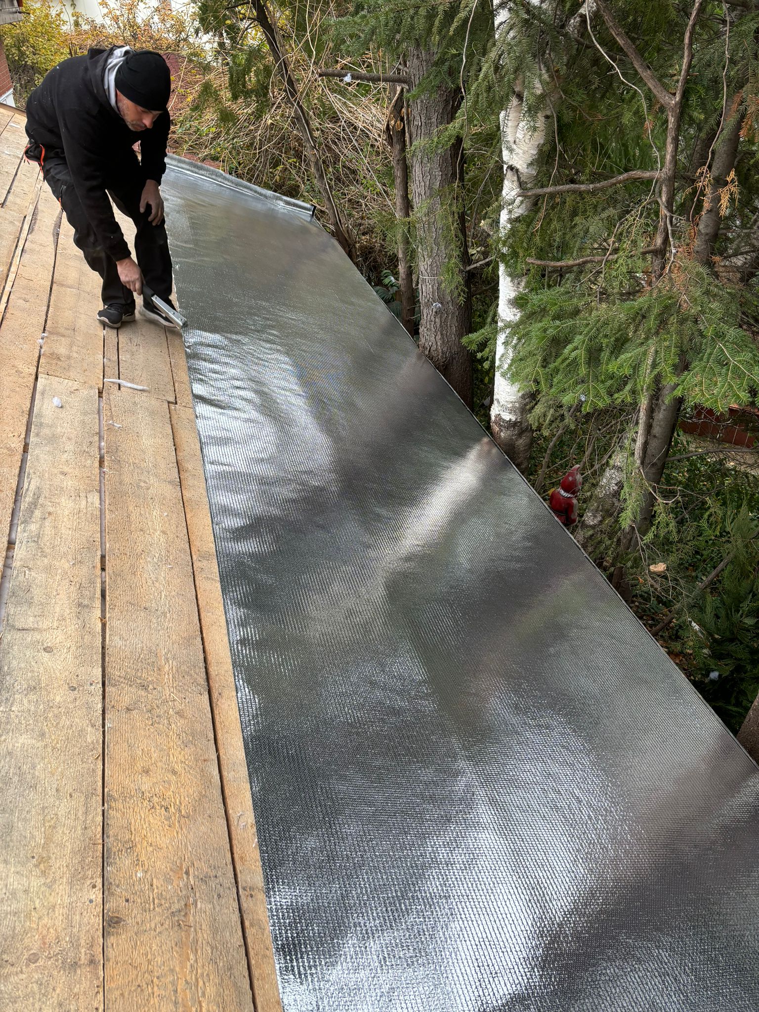 Fixarea foliei anticondens Isoflect Roof Eco pe astereala acoperișului — montatorul aliniază marginea fâșiei reflective înainte de prindere
